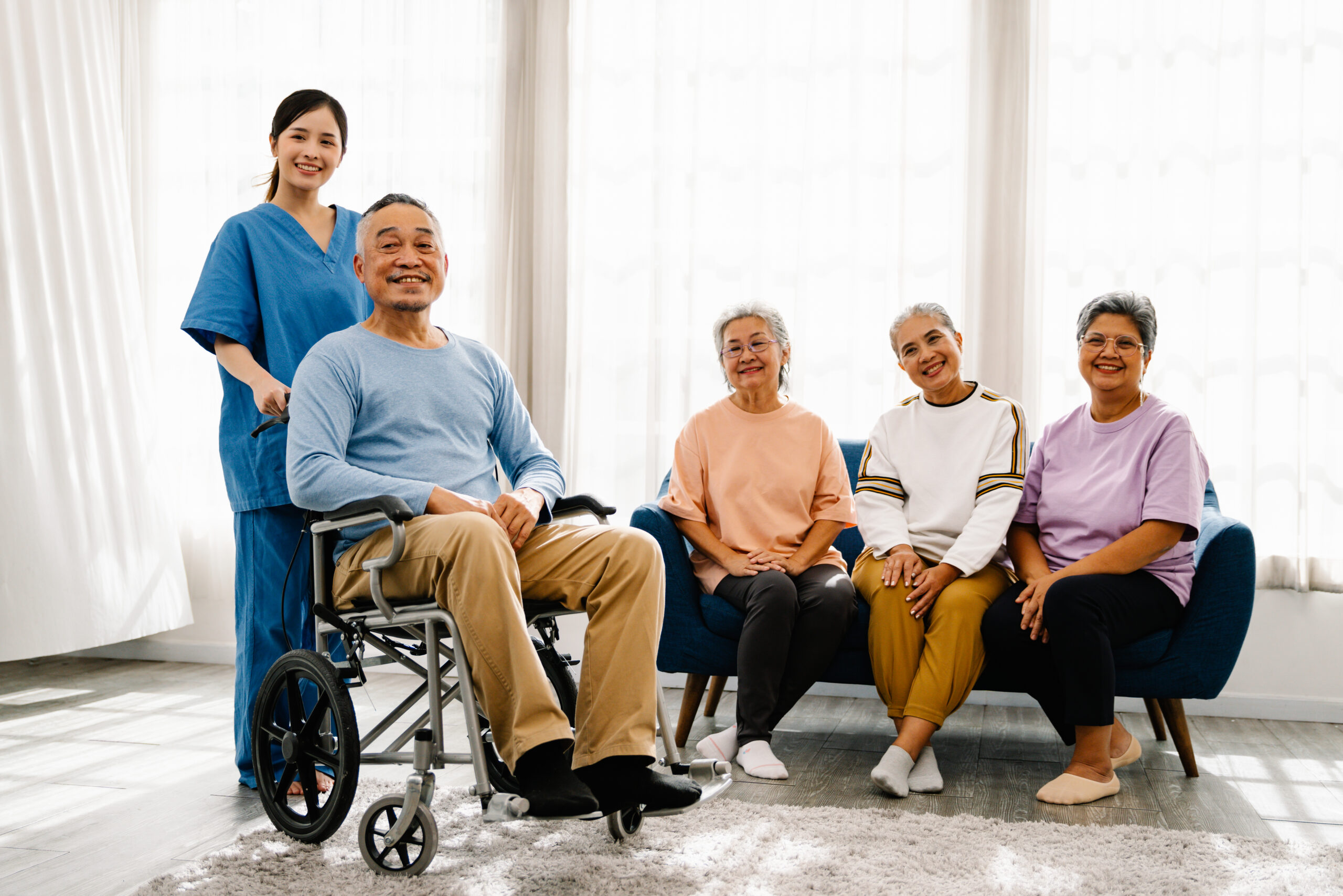 asian senior man patient in wheelchair with young female caregiver or nurse and friends, elderly healthcare concept