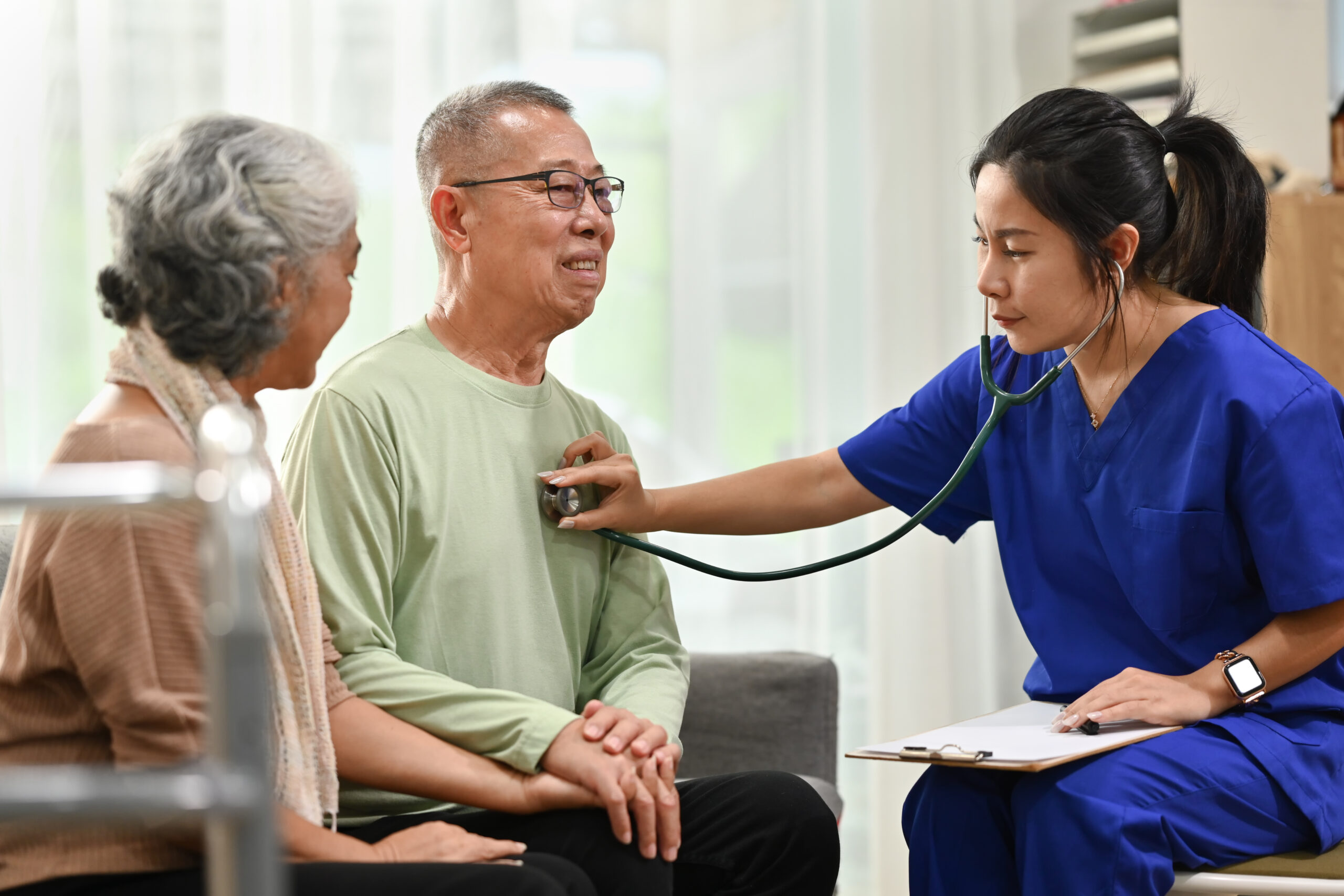 female doctor using stethoscope examining senior male during home care visit. elderly healthcare concept